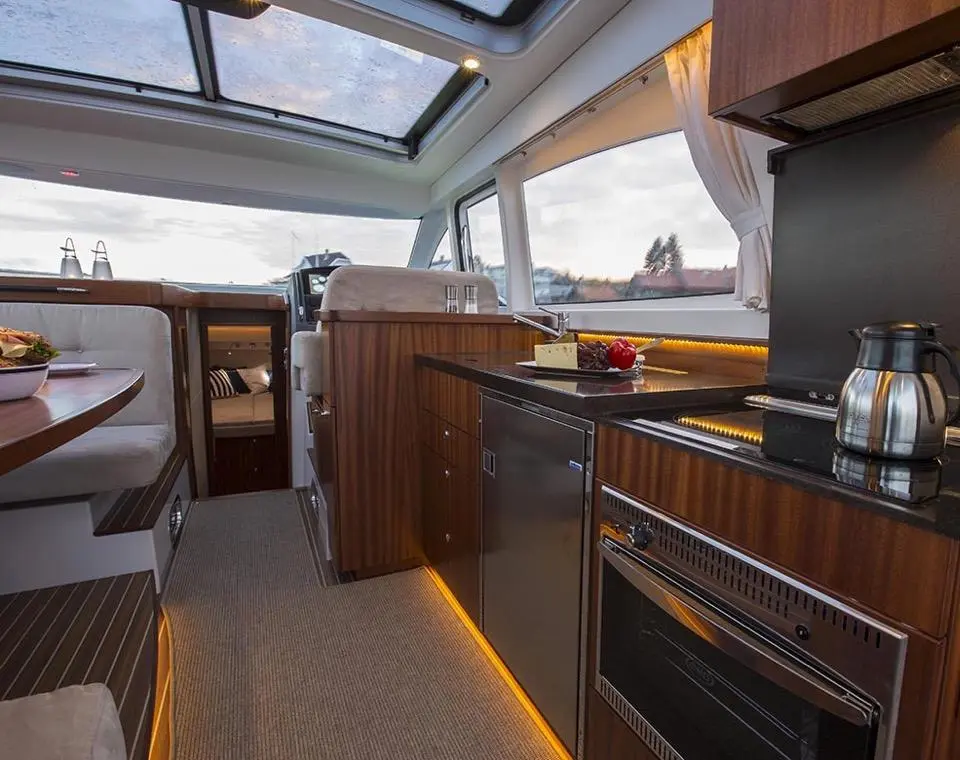 Modern boat interior featuring a sleek kitchen with a dining area, including polished surfaces and ambient lighting.